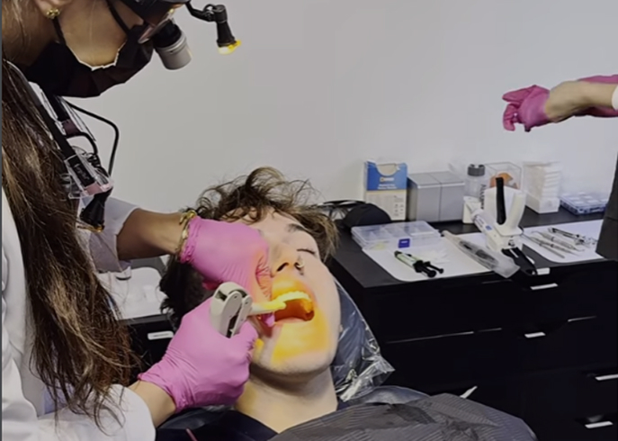 Dentist performing a dental procedure on a patient using a curing light in a dental clinic.