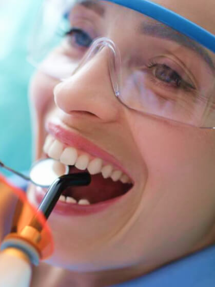 Close-up of a smiling patient wearing protective glasses during a dental procedure.