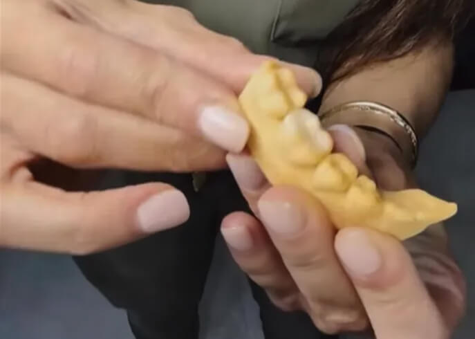 Close-up of hands holding and examining a small, pale yellow, dental imprints